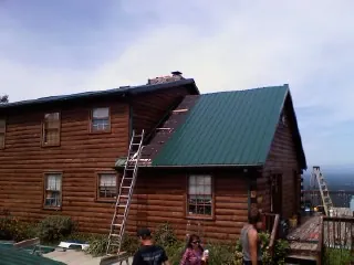 Green metal roof going on a two story log home with ladders set in Junction City